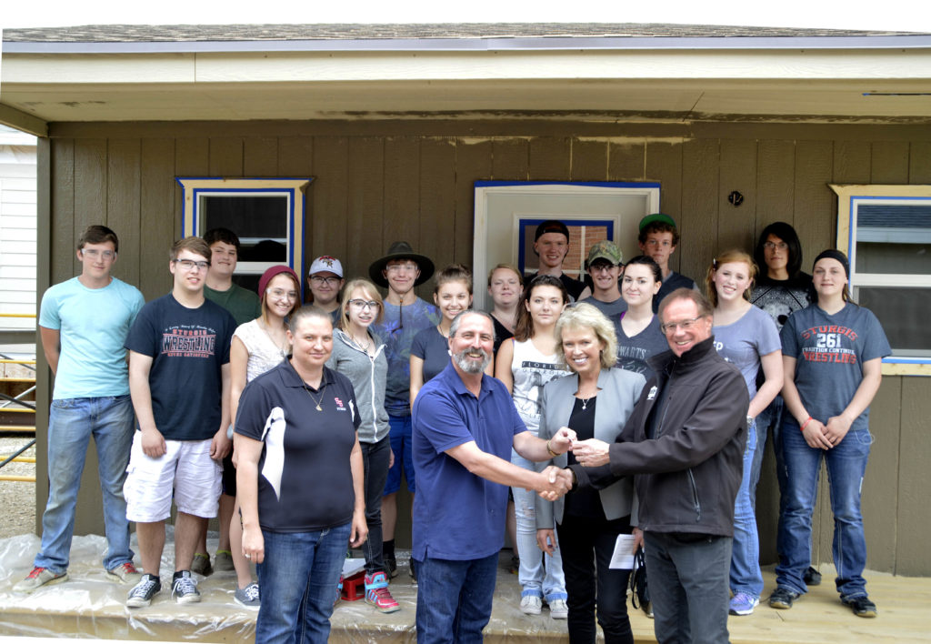 Sturgis Brown High School geometry-in-construction instructor Jon Swan, second from left, hands over the keys for the camping cabins to Buffalo Chip Campground owner Rod Woodruff for whom the students built the two structures. Also pictured, in the front, are Deb Cano, left, SBHS geometry teacher, and Nyla Griffith, media/public relations for Buffalo Chip. Also present for the key exchange were the SBHS students who built the cabins. (Photo by Kris Hubbard/Meade School District)